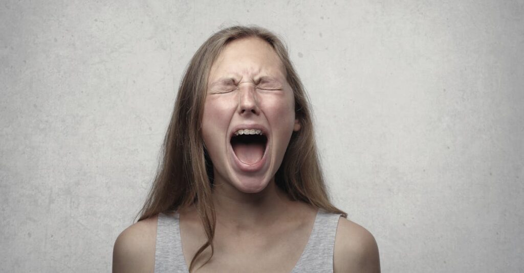 Young woman screaming with emotion, showing braces, against a gray backdrop.